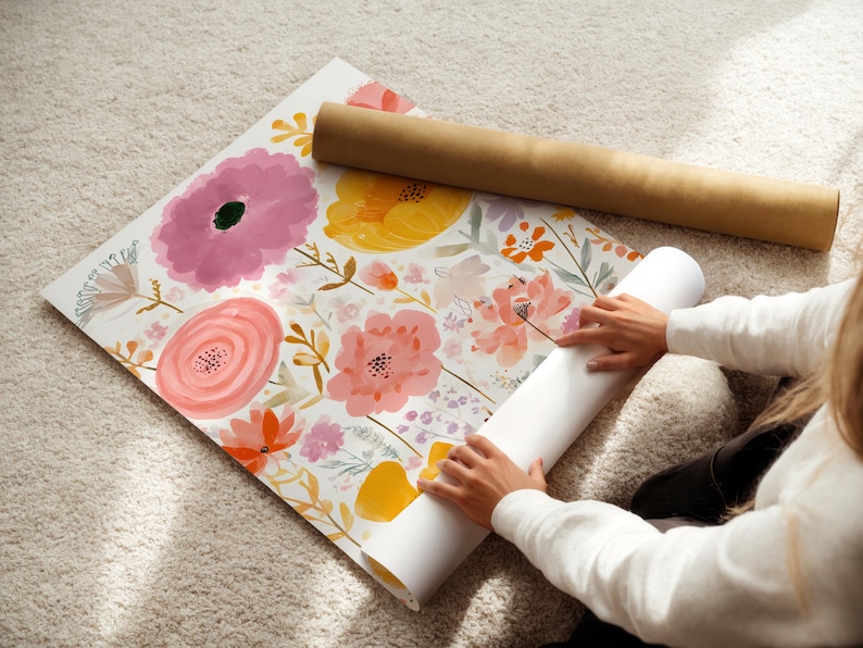 May include: Floral wallpaper roll with a watercolor design featuring pink, yellow, and orange flowers. A brown cardboard tube rests on top. The wallpaper is unrolled on a light-colored carpet.