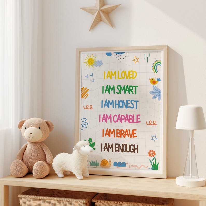 May include: A framed print with the words "I AM LOVED, I AM SMART, I AM HONEST, I AM CAPABLE, I AM BRAVE, I AM ENOUGH" in colorful text. The print has whimsical illustrations of a sun, clouds, and a bird. A teddy bear and a stuffed lamb are on a shelf.