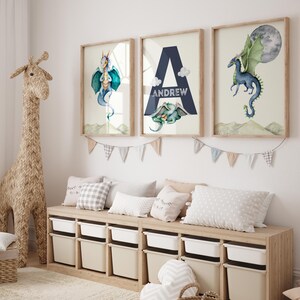 May include: Three framed watercolor prints featuring a blue dragon, the letter A with the name Andrew, and a blue dragon flying with a green moon. The prints are hanging on a white wall above a wooden bench with storage bins.