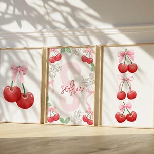 May include: Three framed prints with a pink and white cherry theme. The center print features the name "sofia" in a pink circle with cherries and leaves around it. The prints are perfect for a child's room.