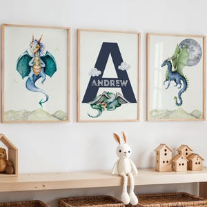 May include: Three framed prints featuring watercolor illustrations of blue dragons. The middle print has the letter A in navy blue with the name Andrew written below it.