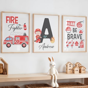Puede incluir: Tres impresiones enmarcadas con temática de bomberos. La primera impresión presenta un camión de bomberos rojo con las palabras "FIRE Fighter". La segunda impresión presenta una gran letra "A" con un bombero sosteniendo una manguera y el nombre "Andrew" debajo. La tercera impresión presenta una boca de incendios, una escalera, una manguera y las palabras "BE BRAVE".