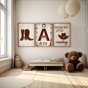 May include: Three brown and white framed prints with a cowboy theme. The left print features a pair of brown cowboy boots. The middle print features the letter A with the name Andrew and cowboy-themed illustrations. The right print features the text "Dream Big Little Cowboy".