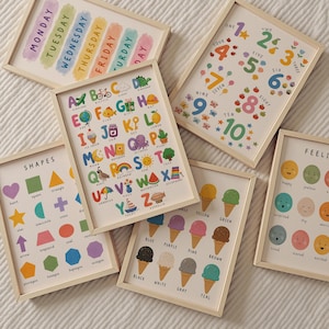 May include: A collection of framed educational prints. The prints feature colorful illustrations of the alphabet, numbers, shapes, days of the week, ice cream flavors, and emotions. Each print is in a light wood frame.