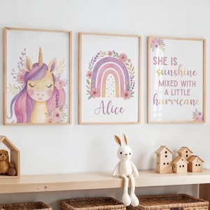 Puede incluir: Tres impresiones artísticas enmarcadas con un tema caprichoso. Una presenta un unicornio con cabello morado y detalles florales. Otra muestra un arcoíris con el nombre "Alice". La tercera impresión dice "She is sunshine mixed with a little hurricane."