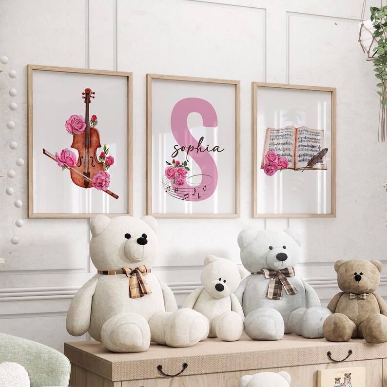 May include: Three framed prints with watercolor illustrations of a violin, the letter S with the name Sophia, and a book with a feather.  The prints are hanging on a white wall above a wooden shelf with four teddy bears.
