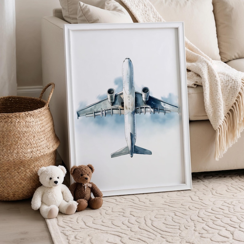 Puede incluir: Una impresi&oacute;n art&iacute;stica enmarcada que presenta una vista a&eacute;rea detallada de un avi&oacute;n de pasajeros contra un cielo nublado. La obra de arte est&aacute; en un marco blanco, y la imagen es en tonos grises y azules. Dos osos de peluche y una cesta de mimbre est&aacute;n en primer plano.