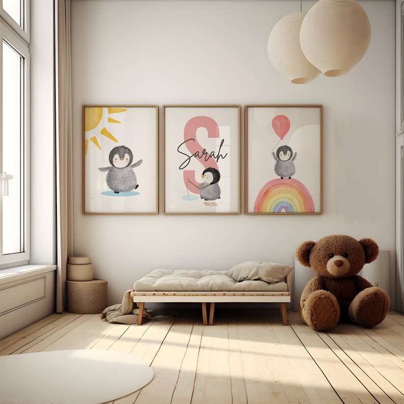 May include: Three framed prints with a penguin theme. The first print features a penguin standing on a white background with a yellow sun behind it. The second print features a pink letter S with the name Sarah written in black. The third print features a penguin standing on a rainbow with a blue balloon in its hand.