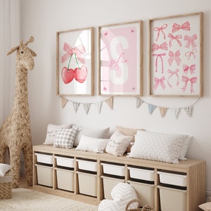 May include: Three framed prints with pink and white designs. The prints feature a cherry with a pink bow, the letter S with the name "Sofia" and a collection of pink bows.
