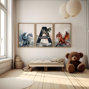 May include: Three framed dragon art prints in a child's room. The prints feature a blue, green, and red dragon. The middle print has the name "ANDREW" with a large letter "A". The room has a wooden floor, a small bed, and a teddy bear.