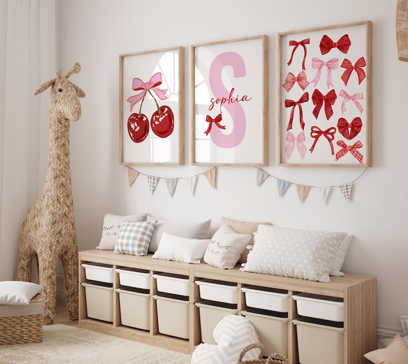 May include: Three framed prints for a child's room. The first print features a pink bow and two red cherries. The second print features a pink letter S with the name "Sophia" written below. The third print features a variety of red and pink bows.