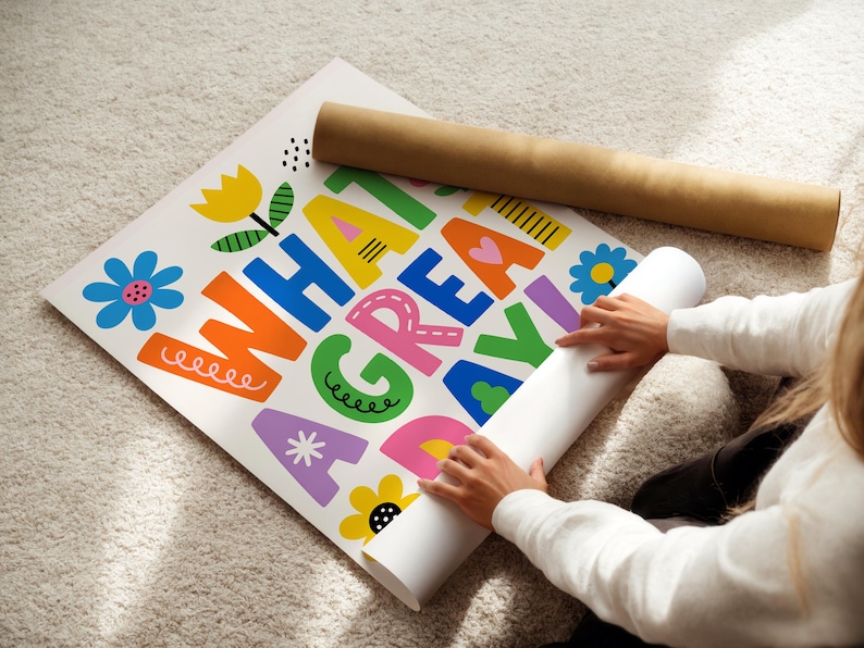 May include: A colorful poster with the words "WHAT A GREAT DAY" in large, playful letters. The poster features floral illustrations and is being unrolled. A brown cardboard tube rests nearby.