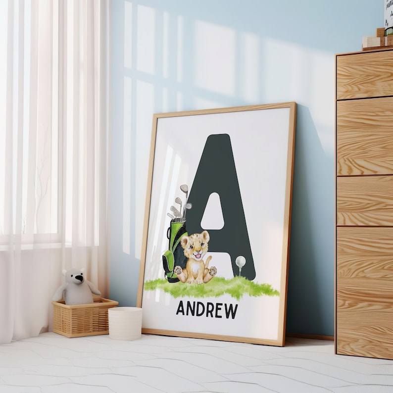 May include: A black letter A with a green golf bag and a small orange lion cub sitting in front of it. The text "ANDREW" is below the letter. The background is white.
