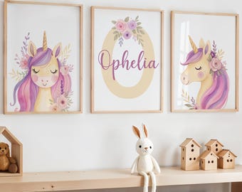 May include: Three framed art prints with watercolour unicorns, purple manes, and floral details. One print displays the name "Ophelia". The prints are displayed above a wooden shelf with decorative items.
