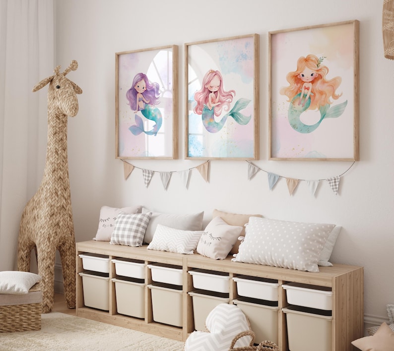May include: Three framed watercolor prints of mermaids with purple, pink, and orange hair. The prints are hung on a white wall above a wooden bench with pillows.
