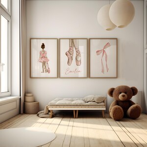 May include: Three watercolor prints featuring a ballerina, a pair of pink ballet shoes, and a pink ribbon bow. The prints are framed in wood and have a white background. The ballerina print includes the name "Emilia".
