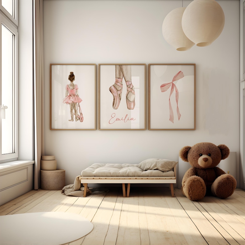 May include: Three watercolor prints featuring a ballerina, a pair of pink ballet shoes, and a pink ribbon bow. The prints are framed in wood and have a white background. The ballerina print includes the name "Emilia".