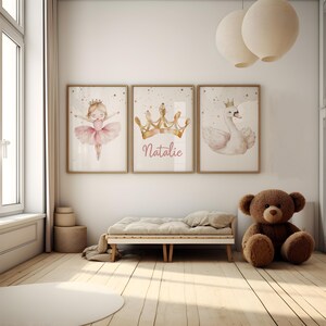 May include: Three framed watercolor prints with a princess theme. One features a ballerina, another a gold crown with the name "Natalie", and the third a swan wearing a crown. The room has a neutral color palette with a teddy bear and a small bed.
