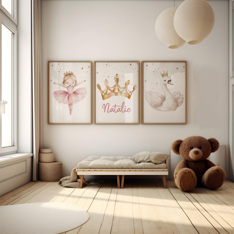 May include: Three framed watercolor prints with a princess theme. One features a ballerina, another a gold crown with the name "Natalie", and the third a swan wearing a crown. The room has a neutral color palette with a teddy bear and a small bed.