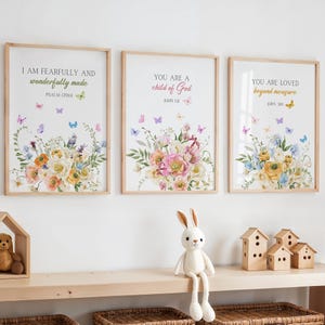 Op de afbeelding: Drie ingelijste kunstprints met inspirerende citaten en bloemstukken. De prints bevatten teksten als "I AM FEARFULLY AND wonderfully made" en "YOU ARE A child of God". Elke print heeft een houten lijst en is versierd met kleurrijke vlinders.
