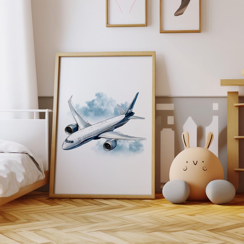 Puede incluir: Un cuadro enmarcado con una ilustraci&oacute;n en acuarela de un avi&oacute;n de pasajeros volando por un cielo nublado. El avi&oacute;n es principalmente blanco con detalles azules. La obra est&aacute; en un marco de madera marr&oacute;n claro, para un dormitorio infantil.