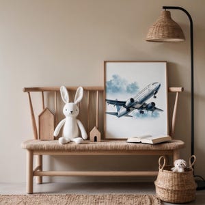 Puede incluir: Una escena interior acogedora con un banco de madera y una impresi&oacute;n enmarcada de un avi&oacute;n azul y blanco despegando. Un conejito de peluche blanco y una peque&ntilde;a cesta con un perro de peluche tambi&eacute;n est&aacute;n presentes.