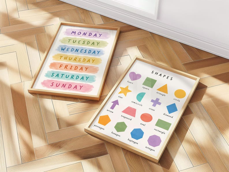May include: Two framed educational prints on a wooden floor. One print displays the days of the week in colorful watercolor brushstrokes. The other print features various shapes with their names, including a heart, star, and diamond.