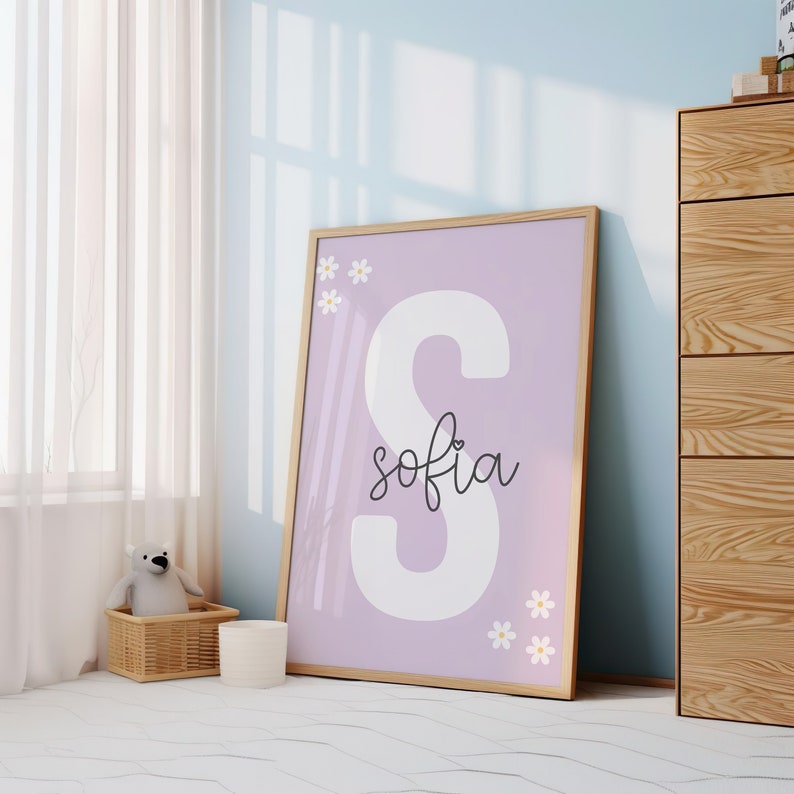 May include: A framed print with a large white letter "S" and the name "sofia" written in cursive on a light purple background. The print is decorated with small white daisies.
