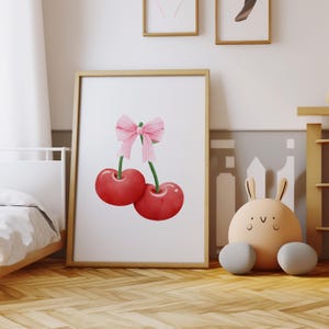 May include: A framed print of two red cherries with a pink bow on the stems. The cherries are against a white background.