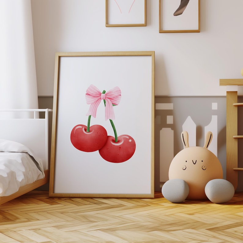 May include: A framed print of two red cherries with a pink bow on the stems. The cherries are against a white background.