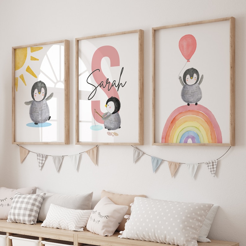 May include: Three framed prints featuring a penguin with a rainbow, a penguin fishing, and a penguin with a sun. The middle print has the name "Sarah" written in black on a pink background.