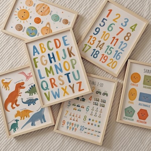 May include: A collection of six framed educational wall art prints featuring watercolor illustrations. The prints display the alphabet, numbers 1-20, numbers 1-10 with icons, various dinosaur species, geometric shapes with faces, and the solar system.