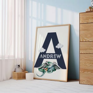 May include: A framed print with a large navy blue letter A and the name Andrew written in white. A green dragon with wings is lying below the letter. The print is on a white background.