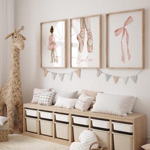 May include: A light wood bench with white storage bins and three pillows. The bench is decorated with a garland of flags and three framed prints. The prints feature a ballerina, a pair of pink ballet shoes, and a pink ribbon.