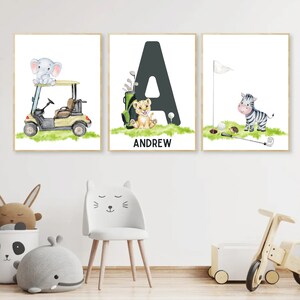 May include: Three framed prints with a white background. The first print features a grey elephant riding in a yellow golf cart. The second print features a black letter A with a lion cub sitting in front of it. The third print features a zebra standing on a green patch of grass with a golf flag and golf clubs. The second print also includes the name "ANDREW" in black text.
