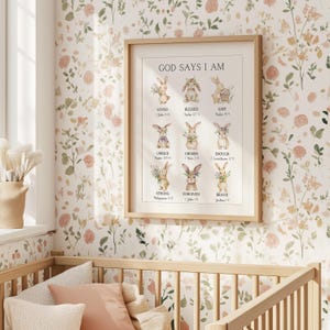May include: A framed print with the text "GOD SAYS I AM" and illustrations of bunnies. The bunnies are depicted with floral accents and are labeled with words like "LOVED", "BLESSED", and "SAFE". The frame is light brown.