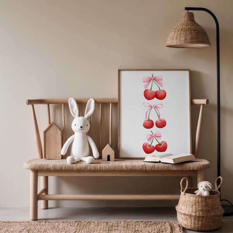 May include: A wooden bench with a white bunny rabbit plush toy sitting on it. A framed print of cherries with pink bows hangs on the wall above the bench. A wicker basket with a stuffed animal sits on the floor next to the bench.