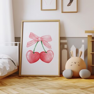May include: A watercolor illustration of two pink cherries tied together with a pink bow. The cherries are on a white background.
