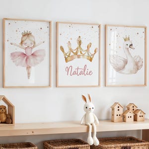May include: Three framed watercolor prints with a princess theme. One features a ballerina in a pink tutu, another a gold crown with the name "Natalie", and the third a swan wearing a crown. The prints are in light wood frames.