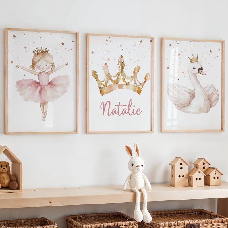 May include: Three framed watercolor prints with a princess theme. One features a ballerina in a pink tutu, another a gold crown with the name "Natalie", and the third a swan wearing a crown. The prints are in light wood frames.