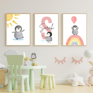 May include: Three watercolor prints featuring a penguin with a sun, a penguin fishing, and a penguin flying with a balloon over a rainbow. The middle print has the name "Sarah" written in pink.