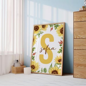 May include: A white background with a large yellow letter S surrounded by sunflowers and small red berries. The name "sofia" is written in cursive below the letter S.