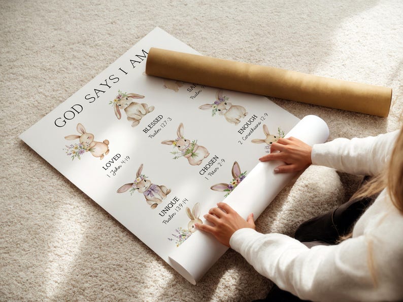 May include: A rolled-up poster with the text "GOD SAYS I AM" and illustrations of bunnies with floral accents. The poster includes words like "LOVED", "BLESSED", "CHOSEN", and "UNIQUE". A brown cardboard tube rests on top.