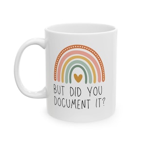 以下が含まれることがあります： パステルカラーの虹のデザインと「BUT DID YOU DOCUMENT IT？」の文字が入った白いセラミックマグカップ。虹にはピンク、黄色、緑、茶色の色合いが含まれています。マグカップにはカーブしたハンドルが付いています。