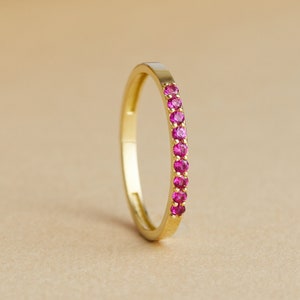 Può includere: Un sottile anello a fascia d'oro con una fila di piccole pietre preziose rosa.