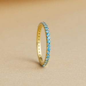 Op de afbeelding: Een gouden ring met een rij kleine, lichtblauwe edelstenen.