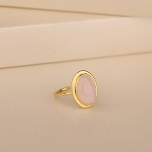May include: A gold ring with a light pink oval gemstone.