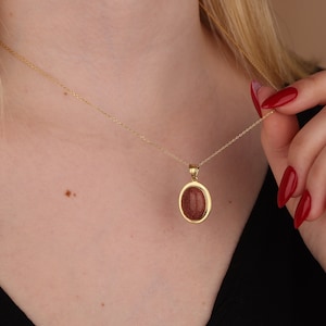 May include: A gold chain necklace with a pendant featuring a reddish-brown oval stone set in a gold frame.