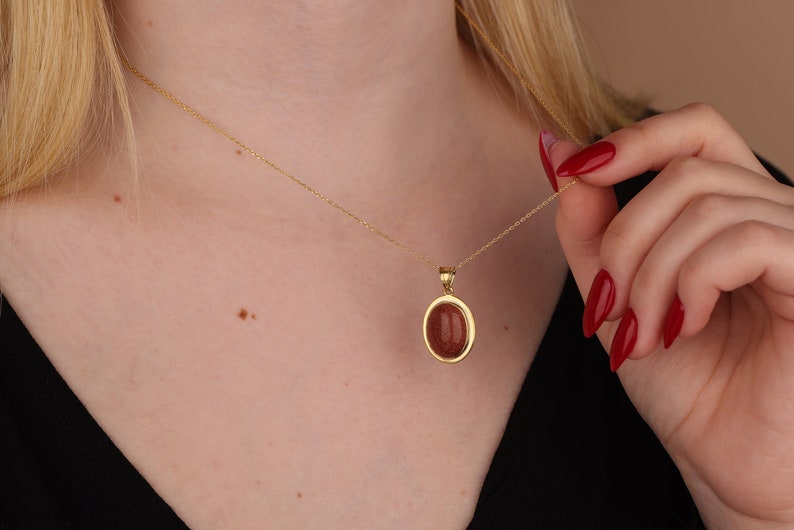 May include: A gold chain necklace with a pendant featuring a reddish-brown oval stone set in a gold frame.