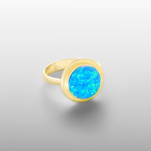 May include: A gold ring with a blue opal gemstone. The ring has a simple band and a bezel setting.